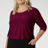 The shirttail hemline adds versatility, making it perfect for both tucked-in and untucked styling. Whether worn under a suit for a polished office look or paired with casual pieces for the weekend, the Jules Top effortlessly transitions with your schedule. Size 18 woman wears her top tucked into black workwear pants.