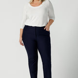 A size 18 woman wears the Lulu tailored pant in Navy. Made in Australia for women. A tailored pant in Navy with waistband and fly front with pockets. Styled back with the Jules. Size inclusive 8 - 24. 