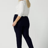 A size 18 woman wears the Lulu tailored pant in Navy. Made in Australia for women. A tailored pant in Navy with waistband and fly front with pockets. Styled back with the Jules. Size inclusive 8 - 24.