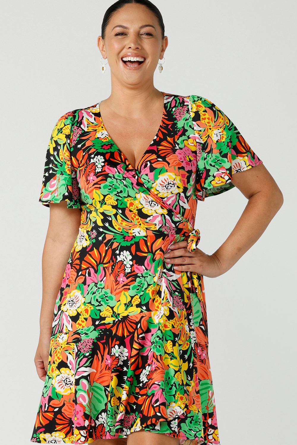 A size 12 happy curvy woman wears a colourful jersey wrap dress in the Cancun print. A petite-height-friendly wrap dress with flutter sleeves and playful ruffle hem, twirl away the summer in the Julie Dress in Cancun. Made in Australia for sizes 8 -24