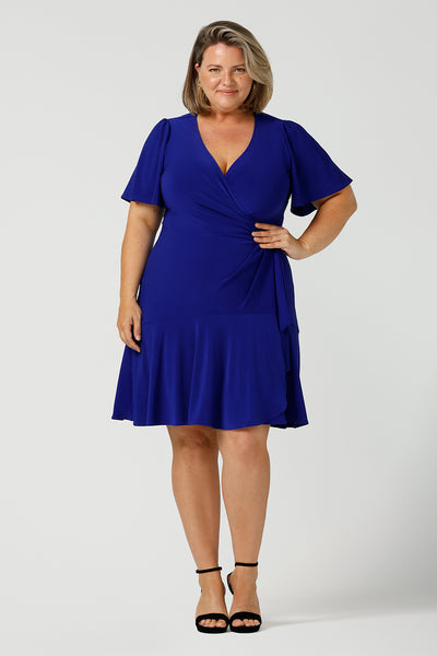 A size 18 plus size woman wears a cobalt blue jersey wrap dress with short flutter sleeves. A good mini length wrap dress for summer, shop Australian-made plus size wrap dresses online at Australian fashion brand Leina & Fleur.