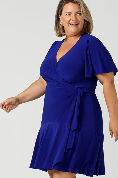 Close up of A size 18 plus size woman wears a cobalt blue jersey wrap dress with short flutter sleeves. A good mini length wrap dress for summer, shop Australian-made plus size wrap dresses online at Australian fashion brand Leina & Fleur.