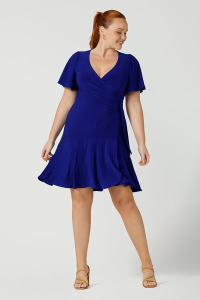A curvy size 12 woman wearing a cobalt blue jersey mini wrap dress with flutter sleeves. A good wrap dress for summer, shop Australian-made wrap dresses online at Australian fashion brand Leina & Fleur.