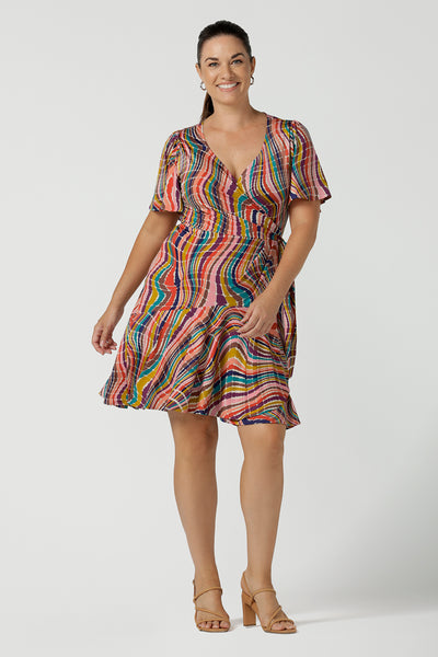 Women in a size 12 wears the Julie wrap dress in Kaleidoscope rainbow stripe. With a tier frill hem and flutter sleeves, this dress is flirty and great for the party season. Made in Australia size 8 - 24.