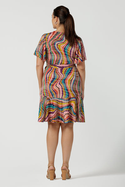 Back view of a women in a size 12 wears the Julie wrap dress in Kaleidoscope rainbow stripe. With a tier frill hem and flutter sleeves, this dress is flirty and great for the party season. Made in Australia size 8 - 24.