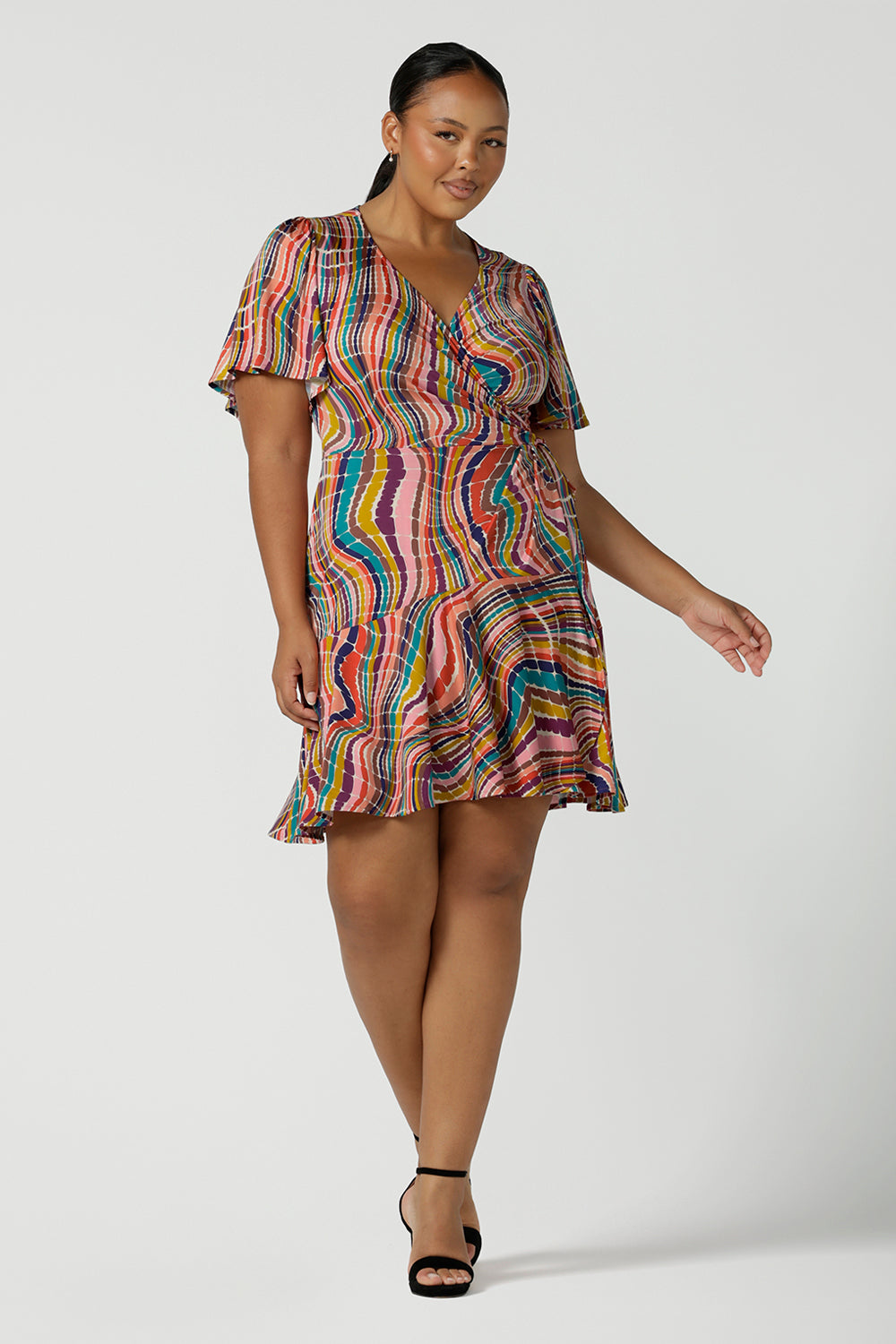 Curvy size 16 woman wears the Julie wrap dress in Kaleidoscope rainbow stripe. With a tier frill hem and flutter sleeves, this dress is flirty and great for the party season. Made in Australia size 8 - 24.