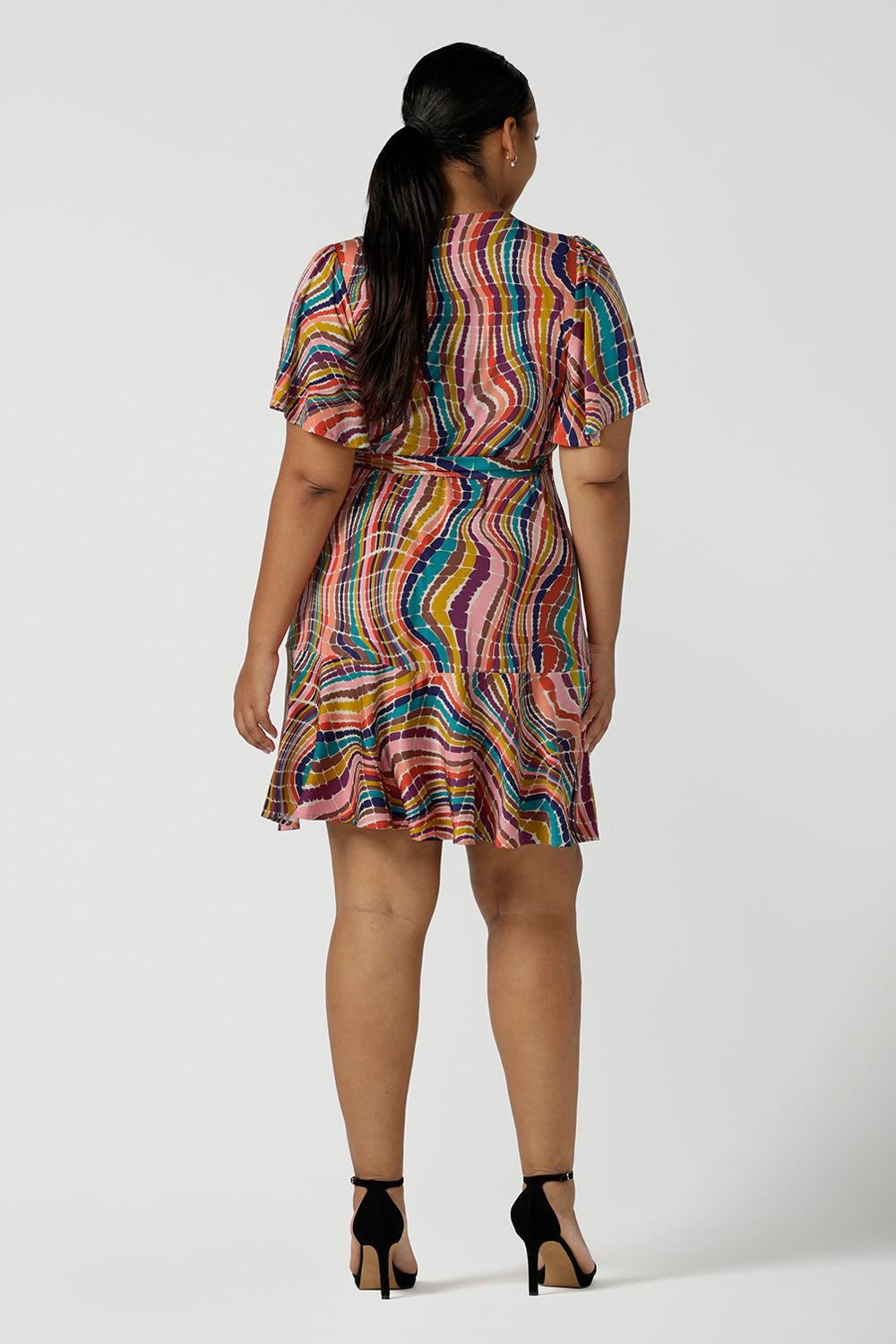 Back view of size 16 woman wears the Julie wrap dress in Kaleidoscope rainbow stripe. With a tier frill hem and flutter sleeves, this dress is flirty and great for the party season. Made in Australia size 8 - 24.