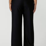 Back view of a good full length trouser for plus size women, these Navy blue, tailored wide leg pants are shown on a size 18, curvy woman. Worn with a short sleeve, white bamboo jersey top, these elegant pants wear for work as smart casual wear. Shop made in Australia trousers for women online at women's clothing brand Leina & Fleur.