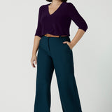 A size 10 woman wears the Yael pant in Petrol. A high waist tailored pant with tailoring elements like side pockets, zip front and belt loops. Full length wide leg pant suitable for comfortable workwear with a statement Petrol colour. Styled back with Vida top in Amethyst. Made in Australia for women size 8 - 24.