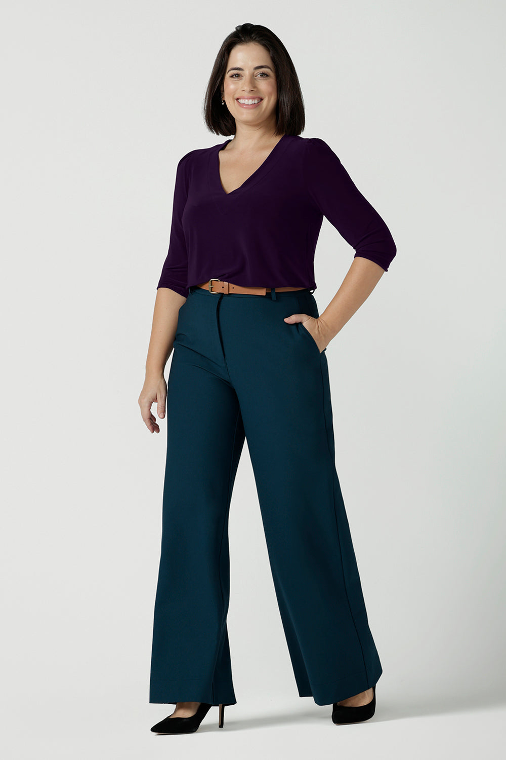 A size 10 woman wears the Yael pant in Petrol. A high waist tailored pant with tailoring elements like side pockets, zip front and belt loops. Full length wide leg pant suitable for comfortable workwear with a statement Petrol colour. Styled back with Vida top in Amethyst. Made in Australia for women size 8 - 24.