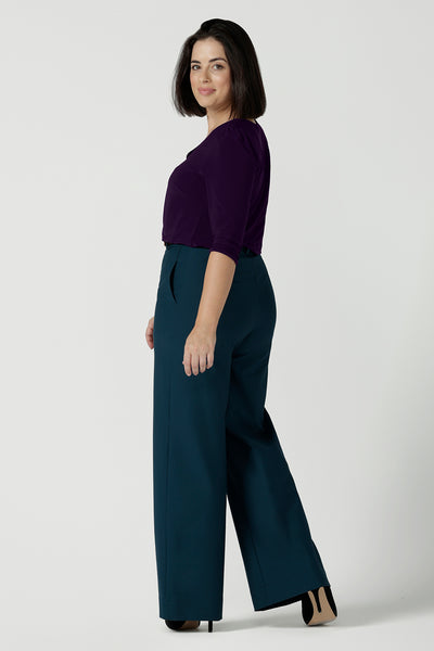 Back view of a size 10 woman wears the Yael pant in Petrol. A high waist tailored pant with tailoring elements like side pockets, zip front and belt loops. Full length wide leg pant suitable for comfortable workwear with a statement Petrol colour. Styled back with Vida top in Amethyst. Made in Australia for women size 8 - 24.