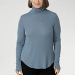 Introducing the Kean high turtleneck top from the Light Layers collection, a stylish and functional piece designed to elevate your wardrobe as the seasons cool. This long-sleeved top features convenient thumb holes for added comfort and warmth. Made from a blend of stretchy Tencel wool fabric, it offers both flexibility and coziness, making it the perfect layering piece for cooler weather.