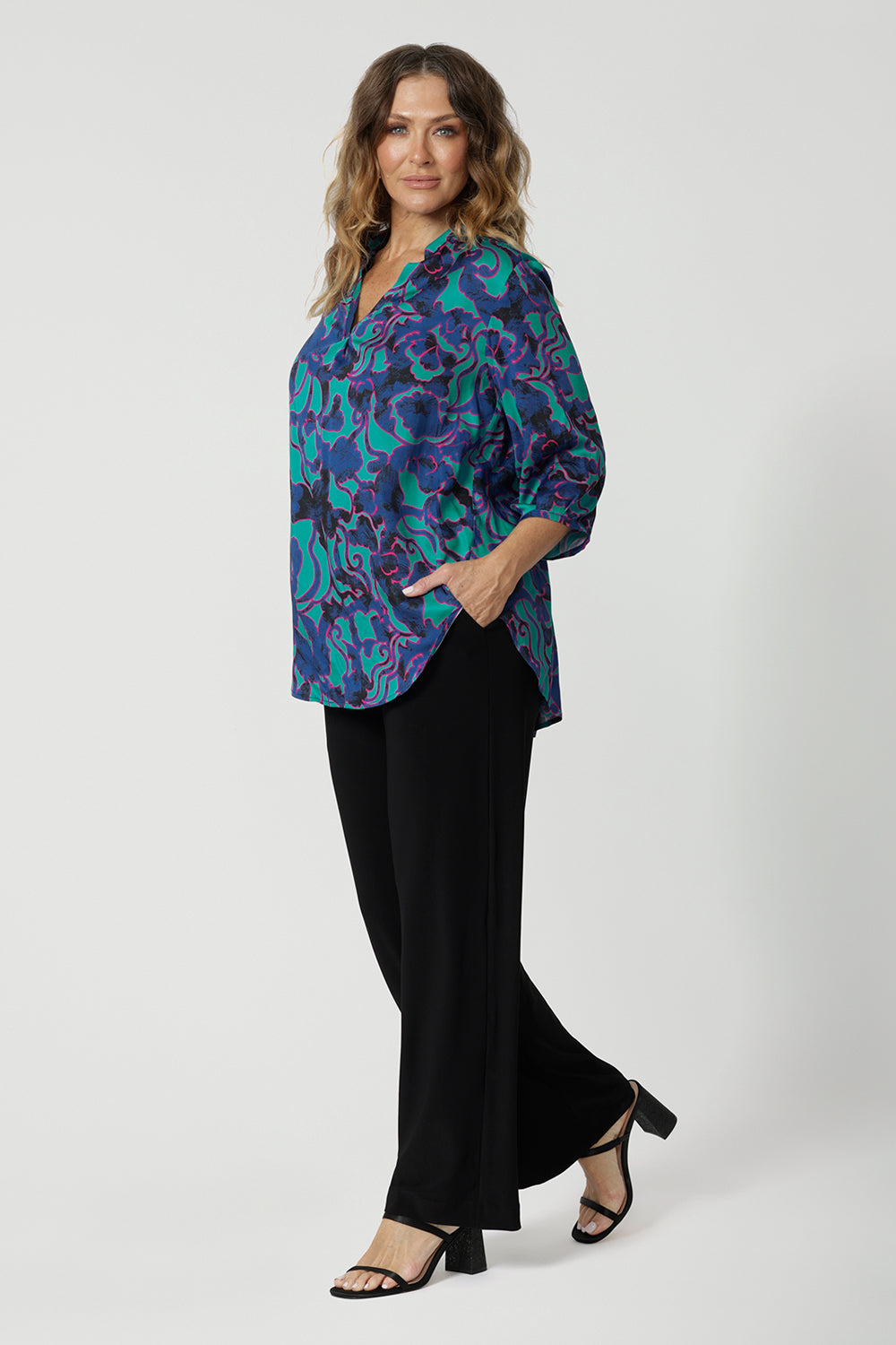 Full body front image of an over 40 year old average height woman, wearing a collared light weight shirt with fabric colours aqua, navy and pink. Shirt has 3/4 sleeves, v neck and collar. This casual shirt is breathable and Australian made. Made by woman in Australia and New Zealand. Leina and Fleur is a woman’s clothing brand that has sizes ranging from 8 to 24 including plus sizes and petite sizes. 