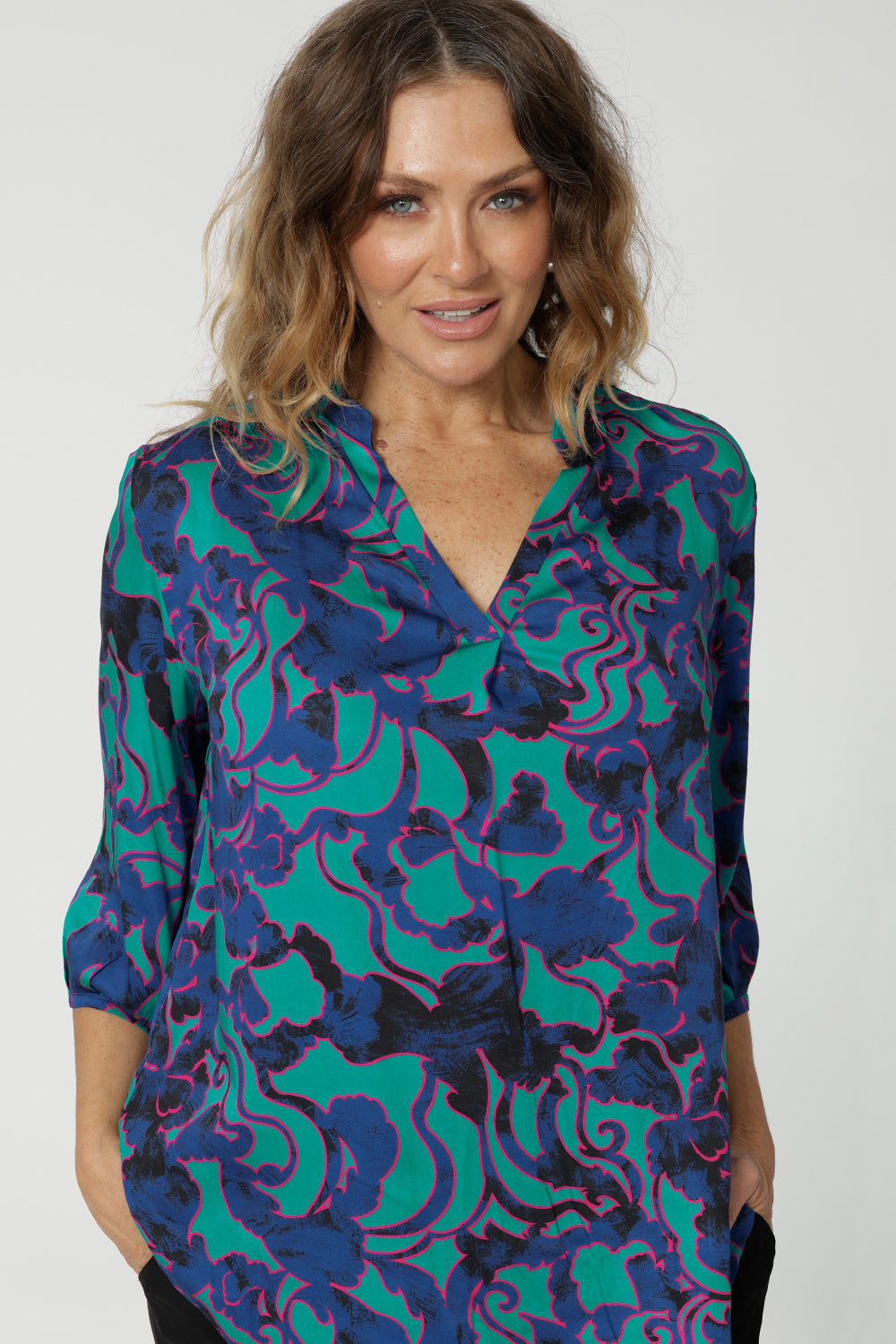 Close up front on image of an over 40 woman wearing an abstract coloured shirt made of comfortable satin rayon. The fabric displays colours of aqua, navy and pink. This lightweight shirt is made by Australian and New Zealand women. Leina & Fleur is an Australian woman’s clothing brand that stocks sizes from 8 to 24. Shop this comfortable blouse in petite and plus sizes. 