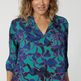 Close up front on image of an over 40 woman wearing an abstract coloured shirt made of comfortable satin rayon. The fabric displays colours of aqua, navy and pink. This lightweight shirt is made by Australian and New Zealand women. Leina & Fleur is an Australian woman’s clothing brand that stocks sizes from 8 to 24. Shop this comfortable blouse in petite and plus sizes. 