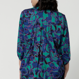 Back view of petite woman wearing a breathable fabric shirt made of satin rayon. Abstract pattern shirt has many colours such as aqua, pink and cobolt blues. This comfortable shirt is Australian made by Australian and New Zealand women. Leina & Fleur is a woman’s clothing label that stocks sizes from 8 to 24. Shop this comfortable blouse in plus size and petite sizes. 