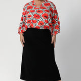 The standout feature of the Kelyn Top is the exaggerated floaty swing back with pleat details, which adds dimension and flow to the piece, creating movement with every step. Plus size woman wears swing shirt with black midi skirt and nude heels for an elevated workwear outfit. Available in sizes 8-24.