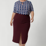 Featuring elbow-length sleeves, this top provides just the right amount of coverage while maintaining a relaxed and chic look. The stitching detail around the front-facing, complemented by thin fabric neckties, adds a tailored touch, perfect for elevating your everyday outfits. Plus size woman wears tie neck top with wine coloured midi skirt and nude heels.