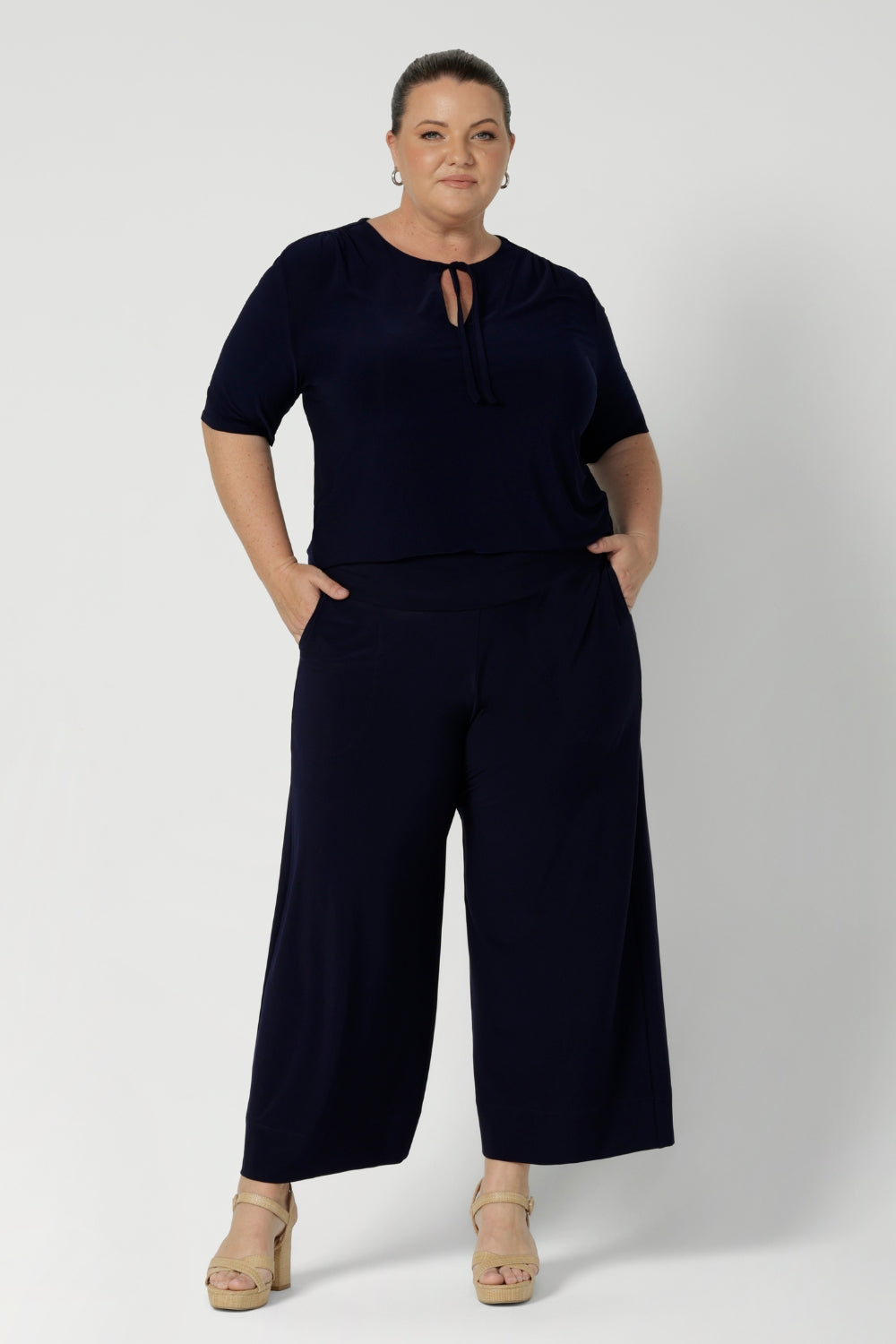 Size 18 model wears elbow sleeve top in navy paired with matching navy pants for an elevated workwear outfit. Available in two elegant colourways. This top also features neck ties that can be adjusted for different looks. Model features neckties tied creating keyhole neckline - for elevated styling. 