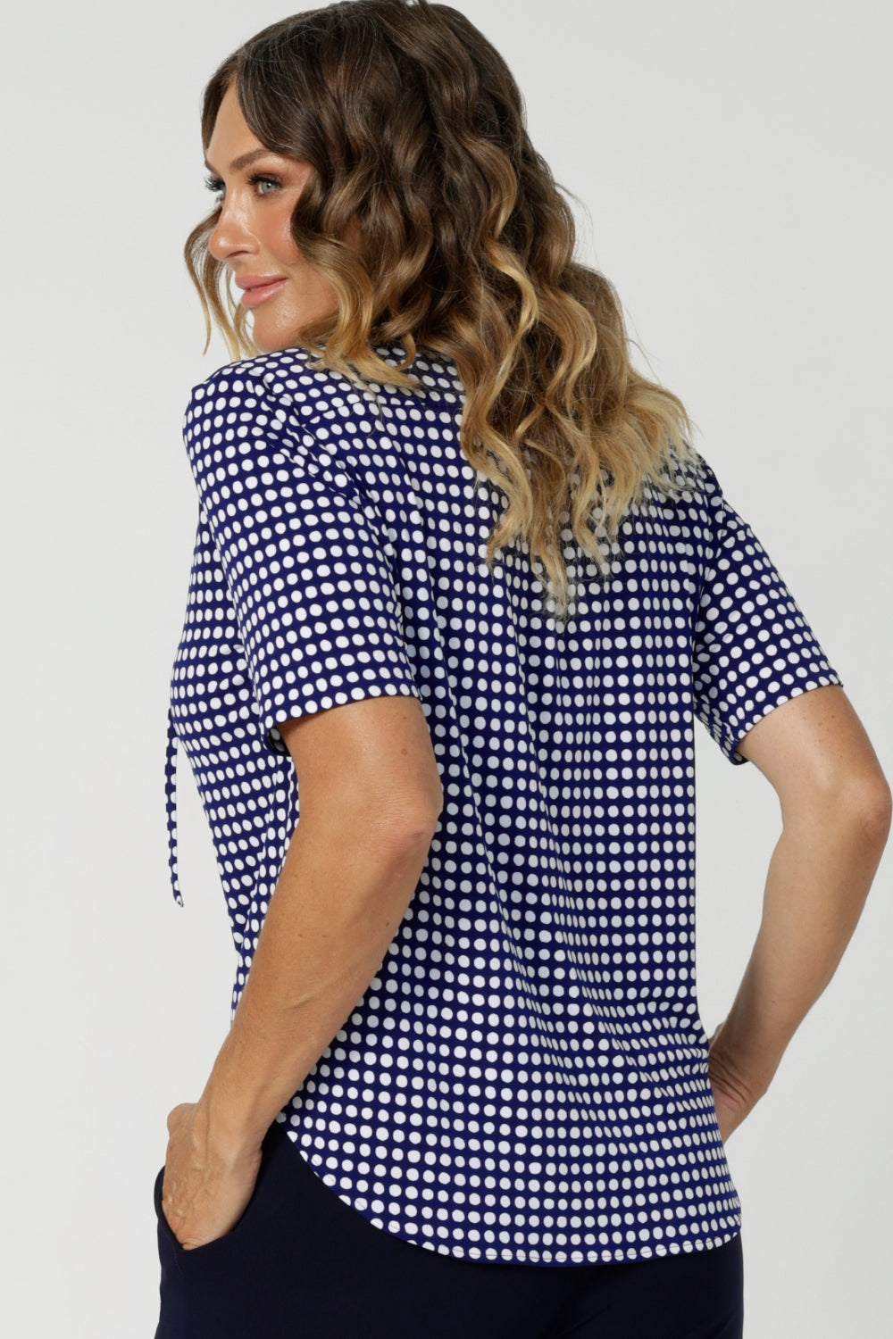 Over 40's woman wears polka dot printed work wear blouse with subtle soft gathers on the shoulders and thin neck ties - creating a tailored feminine shape. Workwear top's shirttail hemline provides a clean, polished finish, making it easy to tuck in or leave out depending on your style preference. Available in size 8-24.