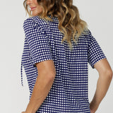 Over 40's woman wears polka dot printed work wear blouse with subtle soft gathers on the shoulders and thin neck ties - creating a tailored feminine shape. Workwear top's shirttail hemline provides a clean, polished finish, making it easy to tuck in or leave out depending on your style preference. Available in size 8-24.