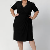 Size 18 woman wears the Kriss dress in black. A functioning wrap work dress in soft black jersey. Great for being comfortable in the office. Made in Australia for women size inclusive fashion 8 - 24.