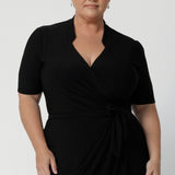 A size 18 woman wears the Kris dress in black. A functioning wrap work dress in soft black jersey. Great for being comfortable in the office. Made in Australia for women size inclusive fashion 8 - 24.