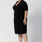 A size 18 woman wears the Kris dress in black. A functioning wrap work dress in soft black jersey. Great for being comfortable in the office. Made in Australia for women size inclusive fashion 8 - 24.