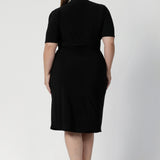 Back view of a size 18 woman wears the Kris dress in black. A functioning wrap work dress in soft black jersey. Great for being comfortable in the office. Made in Australia for women size inclusive fashion 8 - 24.