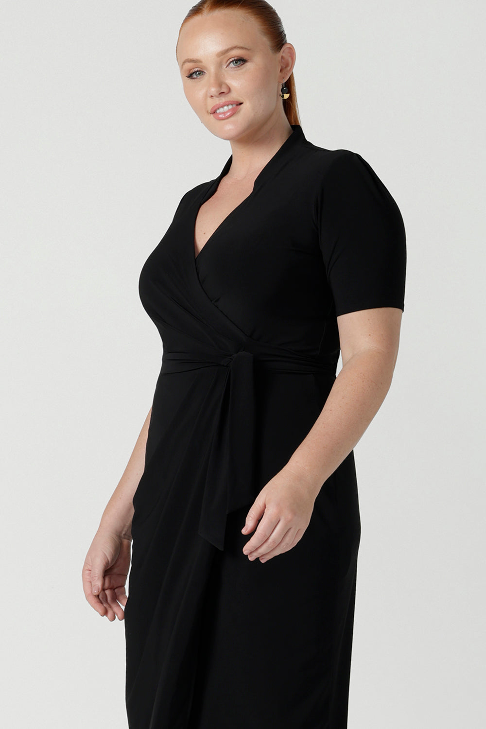 Close up of a size 12 woman wears the Kris dress in black. A functioning wrap work dress in soft black jersey. Great for being comfortable in the office. Made in Australia for women size inclusive fashion 8 - 24.