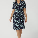 Showing a good wrap dress for work and event wear, a size 12 over 40 woman wears a short sleeve wrap dress in blue floral print. This easy care, jersey wrap dress is made in Australia by Australian and New Zealand women's clothing brand, Leina & Fleur.