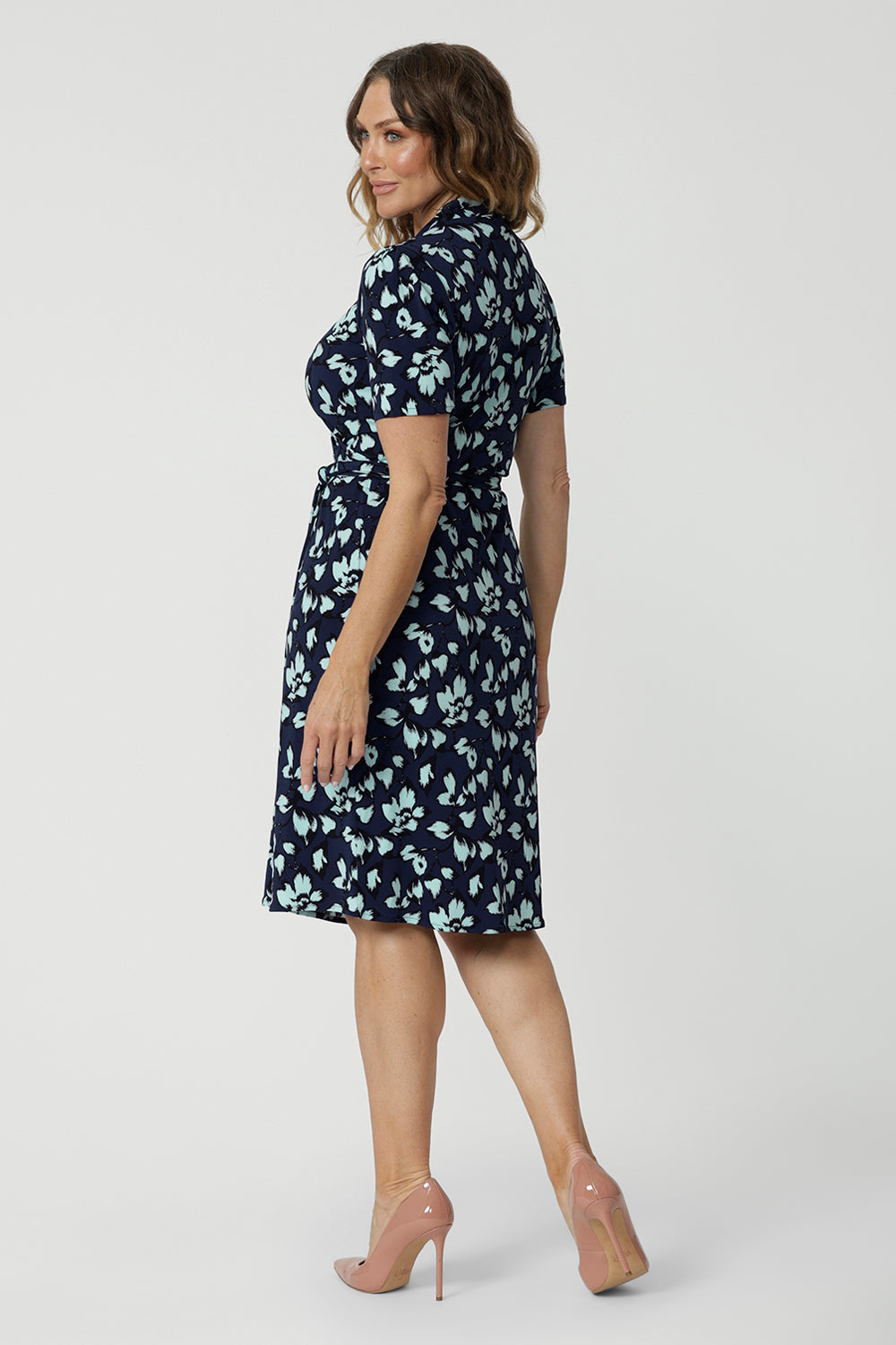 Side view of a good wrap dress for work and event wear, a size 12 over 40 woman wears a short sleeve wrap dress in blue floral print. This easy care, jersey wrap dress is made in Australia by Australian and New Zealand women's fashion brand, Leina & Fleur.