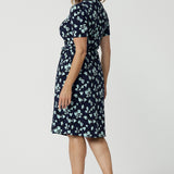 Side view of a good wrap dress for work and event wear, a size 12 over 40 woman wears a short sleeve wrap dress in blue floral print. This easy care, jersey wrap dress is made in Australia by Australian and New Zealand women's fashion brand, Leina & Fleur.