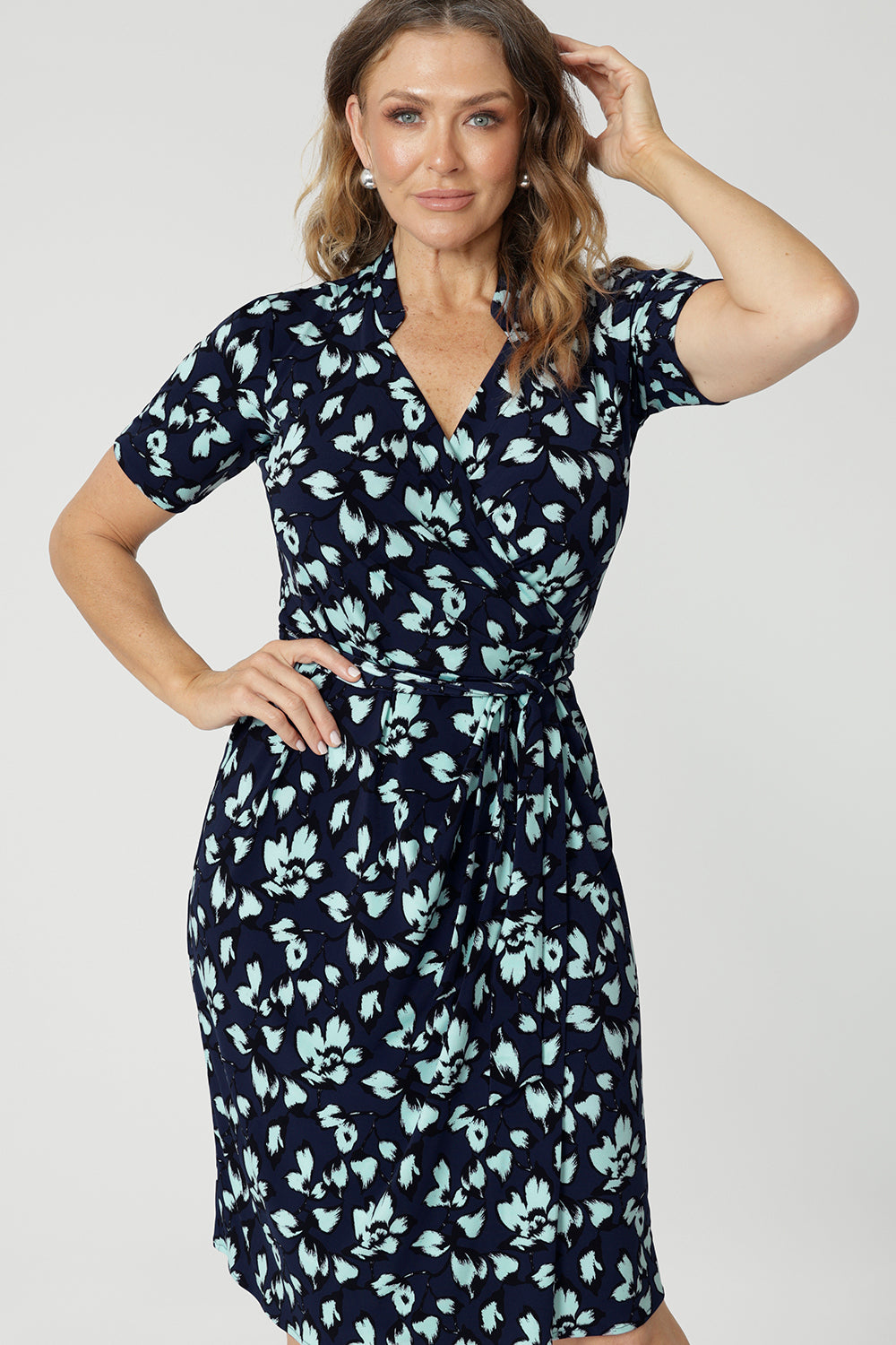 Close up of a good wrap dress for work and event wear, a size 12 over 40 woman wears a short sleeve wrap dress in blue floral print. This easy care, jersey wrap dress is made in Australia by Australian and New Zealand women's clothes label, Leina & Fleur.