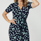 Close up of a good wrap dress for work and event wear, a size 12 over 40 woman wears a short sleeve wrap dress in blue floral print. This easy care, jersey wrap dress is made in Australia by Australian and New Zealand women's clothes label, Leina & Fleur.