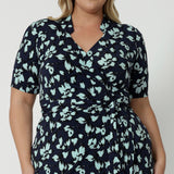 Showing the collar and wrap detail of a good wrap dress for plus size women, a size 18, curvy woman wears a short sleeve wrap dress in blue floral print. This easy care, jersey wrap dress is made in Australia by Australian and New Zealand women's clothing brand, Leina & Fleur.