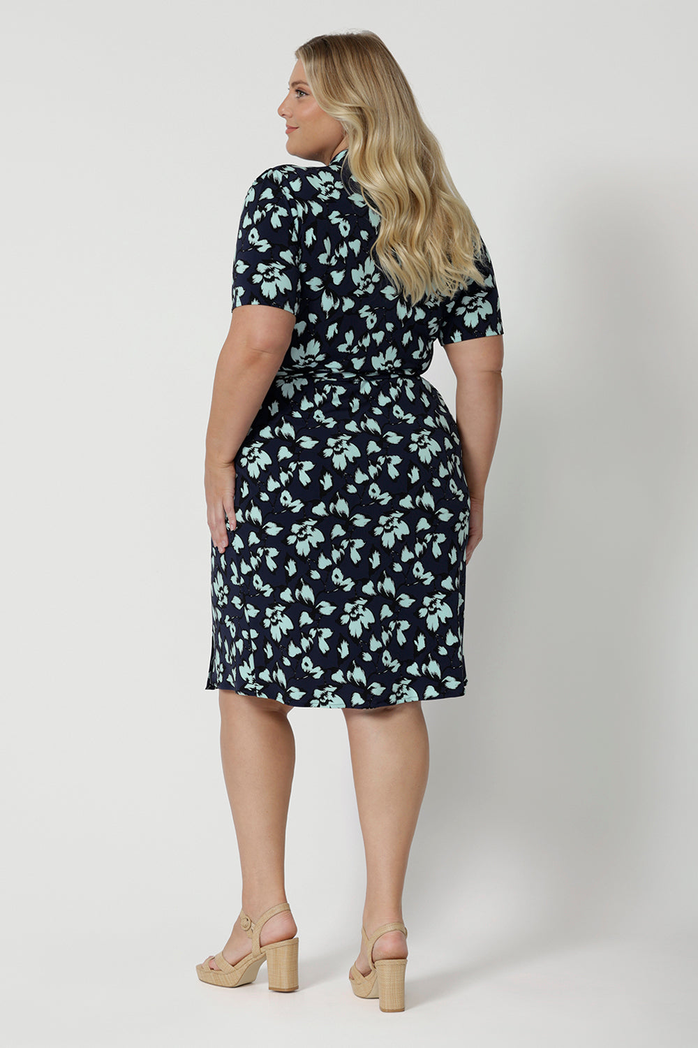 Back view of a good wrap dress for plus size women, a size 18, curvy woman wears a short sleeve wrap dress in blue floral print. This easy care, jersey wrap dress is made in Australia by Australian and New Zealand women's clothing brand, Leina & Fleur.