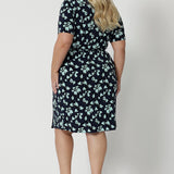 Back view of a good wrap dress for plus size women, a size 18, curvy woman wears a short sleeve wrap dress in blue floral print. This easy care, jersey wrap dress is made in Australia by Australian and New Zealand women's clothing brand, Leina & Fleur.