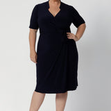 Full body image of a plus sized woman wearing a navy base wrap dress. This collared dress is Australian made for Australian and New Zealand women. Woman’s clothing brand Leina & Fleur stock sizes from 8 to 24 including plus sizes and petite sizes. 