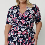 Close up shot of plus sized woman wearing floral wrap dress. The dress design made from easy care dry touch jersey fabric. Printed design has a colourful combination of white and pink roses on navy base. This work wear dress is comfortable, easy and perfect for any travel capsule. Designed in Australia by Australian and New Zealand women. Leina & Fleur is a fashion brand for woman that have sizes from 8 to 24. Shop this functioning wrap dress in petite sizes and plus sizes.