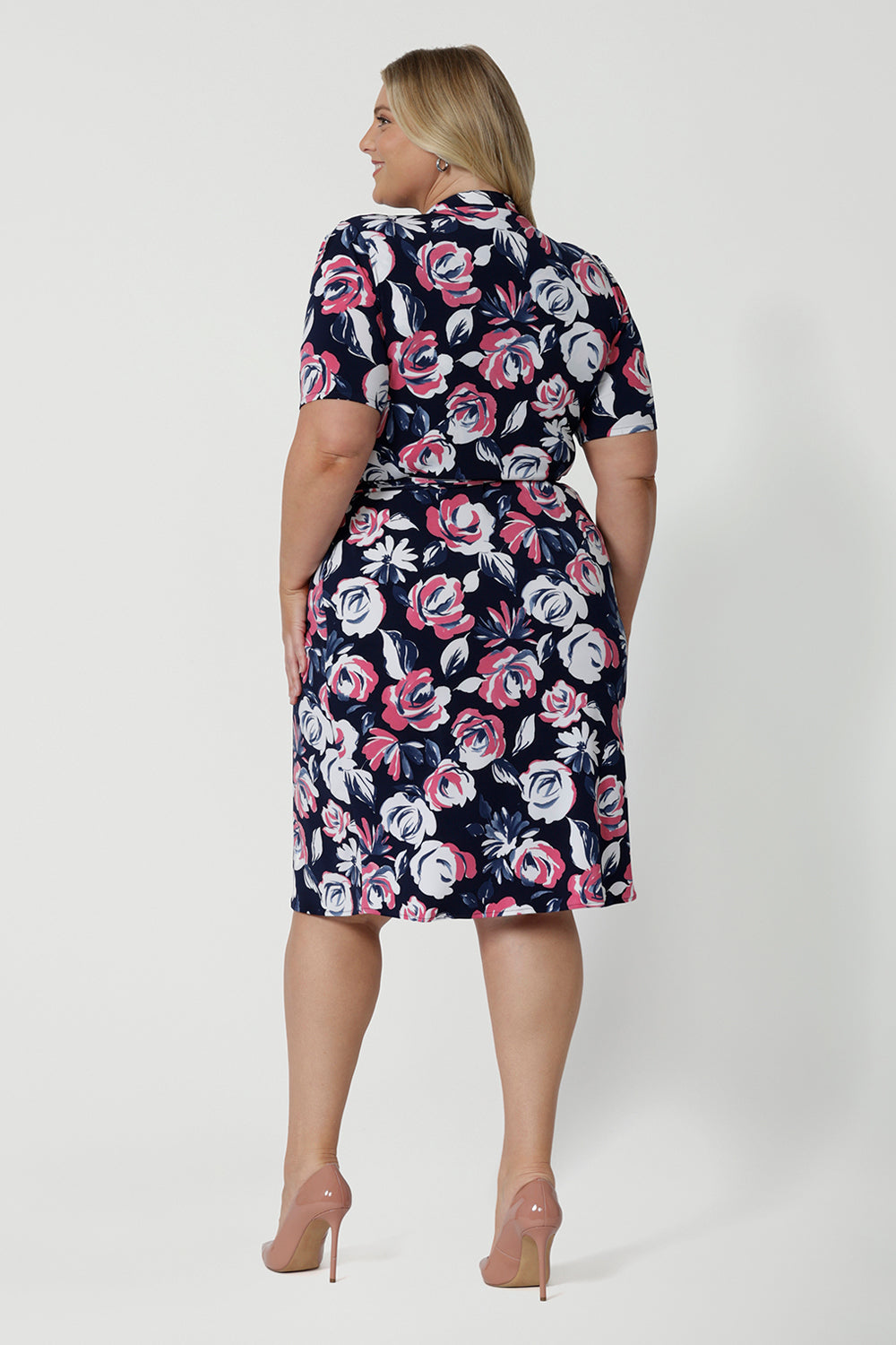 Back shot image of plus sized woman wearing a floral wrap dress. Dress is made from easy care dry touch jersey fabric. Printed design displays white and pink roses on navy. This work wear dress is comfortable, easy and perfect for travel. Outfit designed in Australia by Australian and New Zealand women. Leina and Fleur is a fashion brand for woman that stock sizes from 8 to 24. Shop this functioning wrap dress in petite sizes and plus sizes.