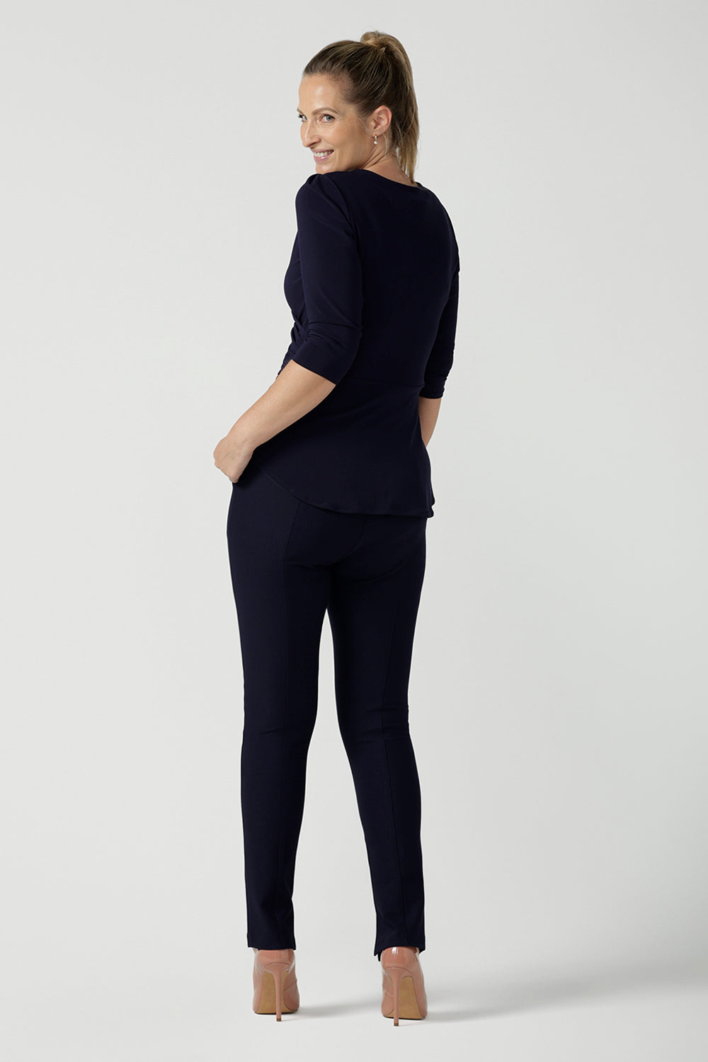 Back view of a size 10 model wears the Kyle Top in Navy made in Australia for women size 8 - 24. A fixed wrap top in Navy with 3/4 sleeves and a fixed wrap. Pleated from and v-neckline. A versatile work to dinner date top. Made in Australia for women size 8 - 24. Styled back with Navy Brooklyn pants.