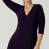 Close up of a size 10 Woman wears the Amethyst Kyra dress in jersey. Made in Australia for women. Beautiful twist front neckline with 3/4 sleeve, high-low hem, empire line. Work wear for women and easy care. Great wedding guest outfit, mother of the bride. Made in Australia for women size 8 - 24.