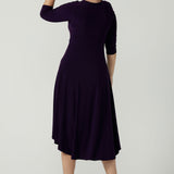 Back view of a size 10 Woman wears the Amethyst Kyra dress in jersey. Made in Australia for women. Beautiful twist front neckline with 3/4 sleeve, high-low hem, empire line. Work wear for women and easy care. Great wedding guest outfit, mother of the bride. Made in Australia for women size 8 - 24.