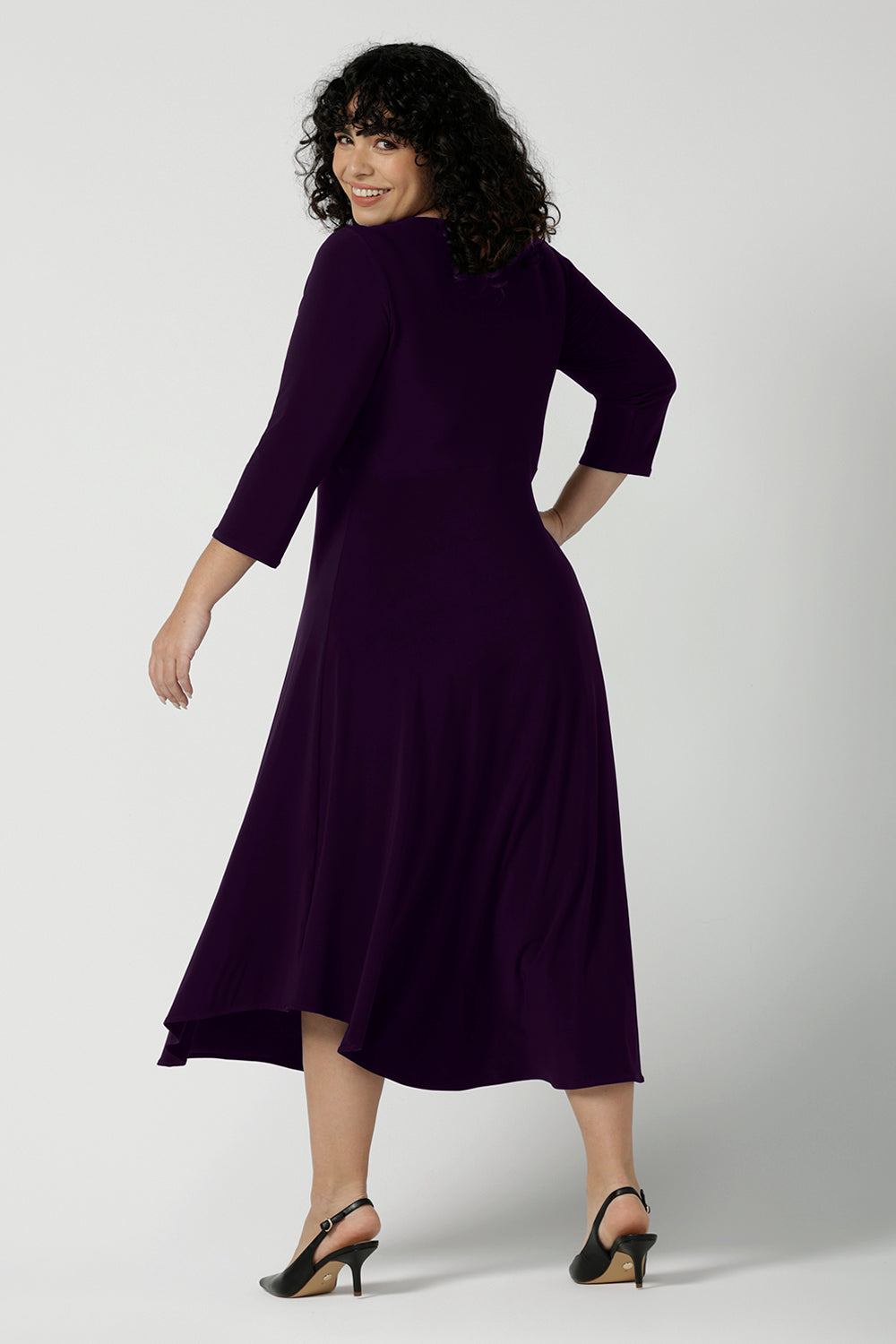 Back view of a size 18 Woman wears the Amethyst Kyra dress in jersey. Made in Australia for women. Beautiful twist front neckline with 3/4 sleeve, high-low hem, empire line. Work wear for women and easy care. Great wedding guest outfit, mother of the bride. Made in Australia for women size 8 - 24.