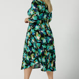 Back view of a size 18 woman wears the Kyra dress in Canopy. A twist front dress with a 3/4 sleeve on a watercolour print. Made in Australia for women size 8 - 24.