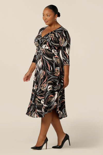 A fuller figure, size 18 woman wears an empire line dress with sweetheart neckline and 3/4 sleeves. Great for work wear, this twist front dress with midi-length skirt looks smart for office dress style.