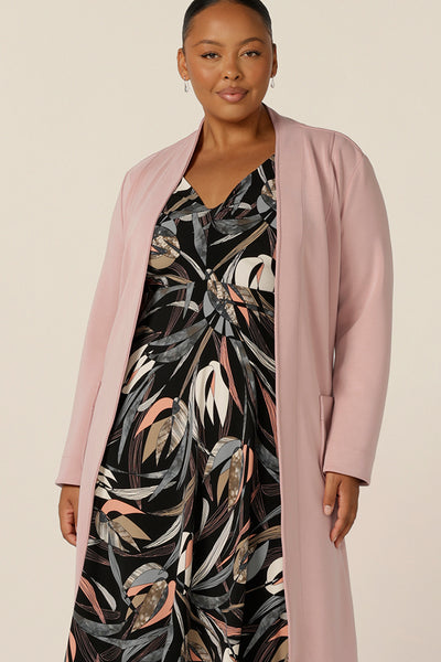 A fuller figure, size 18 woman wears an empire line dress with sweetheart neckline and 3/4 sleeves under a pink modal trenchcoat. Great for work wear, this twist front dress with midi-length skirt looks smart for office dress style.