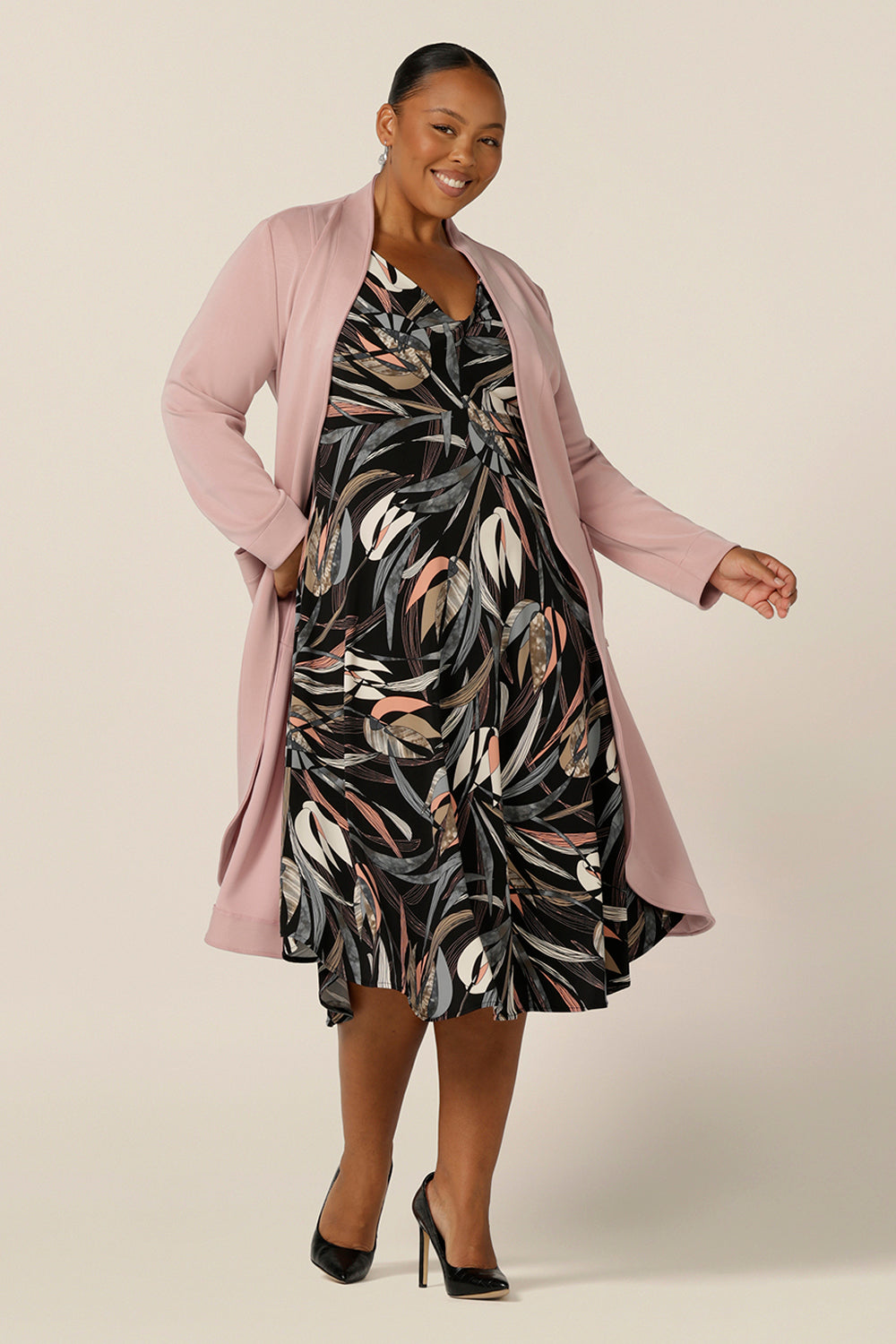 A fuller figure, size 18 woman wears an empire line dress with sweetheart neckline and 3/4 sleeves and pink modal coat. Great for work wear, this twist front dress with midi-length skirt is smart casual office dress style at its best.