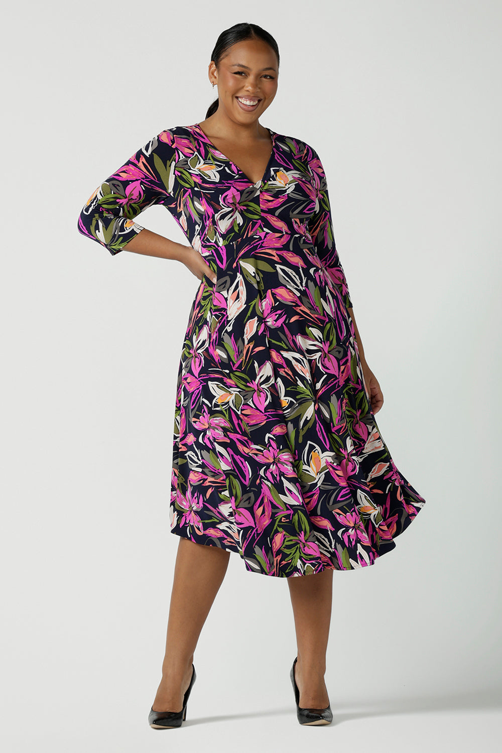A size 16 woman wears a Kyra dress in Vivid Flora. Empire line fit and flare style with a 3/4 sleeve. Twist front neckline. Flattering shape for all sizes 8 - 24. Made in Australia for corporate casual women. 